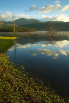 clear reflecting lake, with clouds and a blue sky and mountains in the background