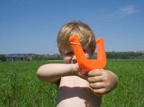 The naughty little boy aims from a slingshot towards the spectator