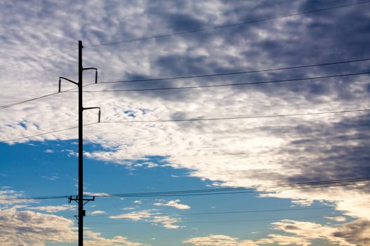 A powerline pole is silhouetted in front of a cloudy sky