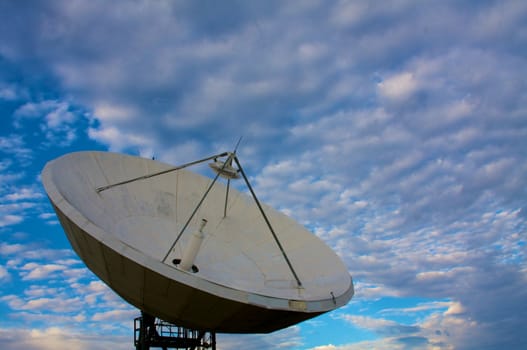 A large satellite dish points into a cloudy blue sky