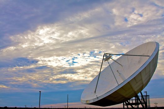 A large satellite dish points into a cloudy blue sky