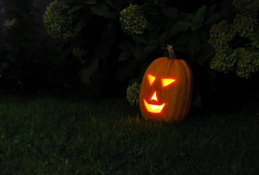 Yellow pumpkin glowing in the dark outside on the grass.