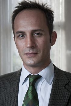 Headshot of white man in a suit with blurred curtain in the background.