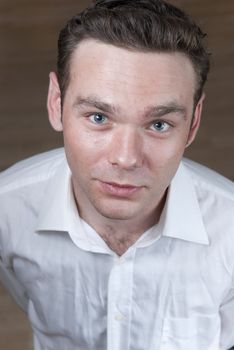 High angle headshot of young white man with wooden board floor in the background.