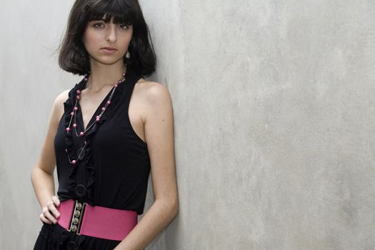 An 18 year old exotic brazilian model, with short dark hair, a young looking face and a skinny body. She is wearing a black dress and pink belt. Plenty of copyspace in the image.