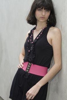 An 18 year old exotic brazilian model, with short dark hair, a young looking face and a skinny body. She is wearing a black dress and pink belt.