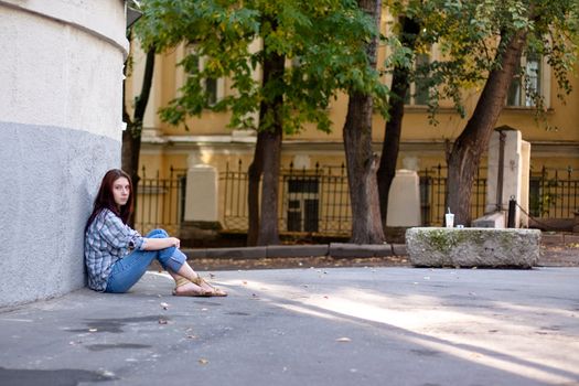 Girl sitting on asphalt near wall

