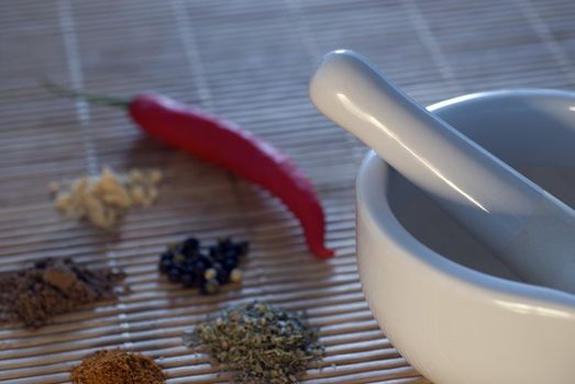 a white pestle and mortar with a selection of spices, narrow depth of field