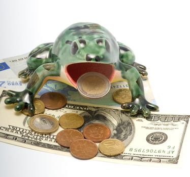 The ceramic frog sitting on money holds in a mouth a coin two euros.