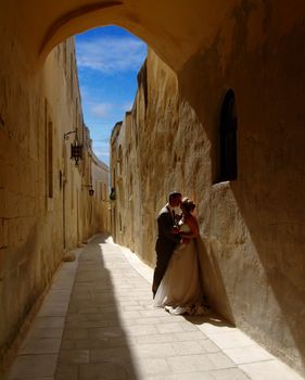 Newsly weds kissing underneath medieval archway in Malta