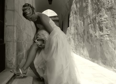 Bride arranging her wedding gown on medieval doorstep