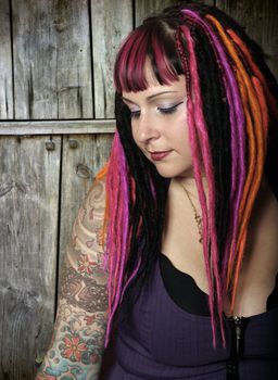 Portrait of a beautiful female goth with dreadlocks in front of an old wooden door.  Slightly desaturated.
