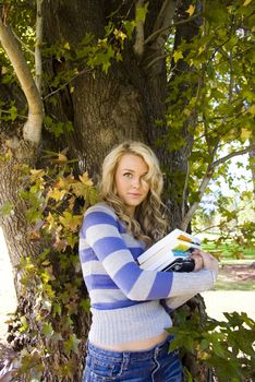 young student with books standing under a tree
