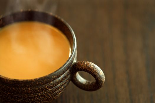 A macro, selective focus image of coffee with milk, in a wooden mug on a wood table.  Lots of copyspace available - Shallow depth of field with the focus on the handle.  Shot with natural light.
