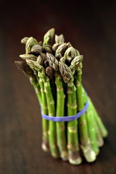 Bunch of asparagus on a wooden table.  Shallow depth of field, focusing on the tips.
