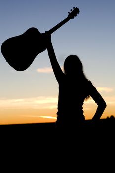 Silhouette of a woman raising her guitar high in the air in confidence or success.