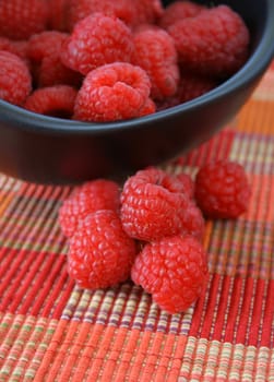 raspberries in a bowl with some laying out side of the bowl

