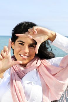 Portrait of beautiful smiling brunette girl framing her face at beach