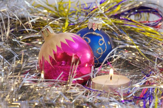 Two round Christmas tree toy among decoration and a candle.