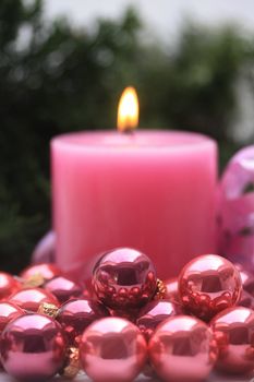 A pink candle and some small pink christmas balls