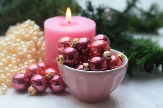 A pink candle and a bowl with small christmas balls