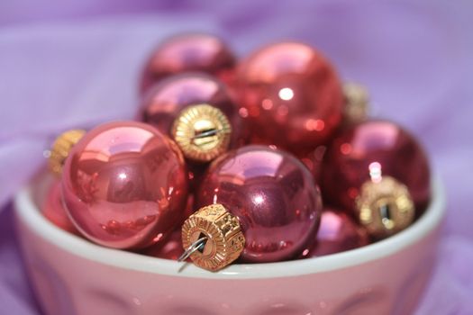 A bowl with pink christmas balls on a purple background