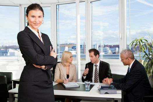 Businesswoman sitting in front. Three business colleagues working in background.