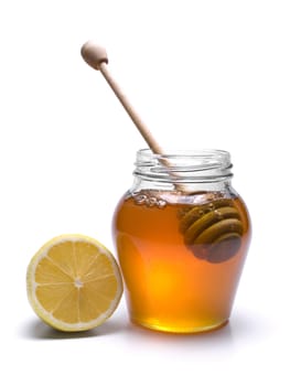 Jar of honey with a wooden drizzler and a lemon. Isolated on white background.