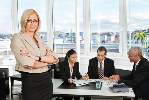 Businesswoman sitting in front. Three business colleagues working in background.