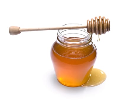 Jar of honey with a wooden drizzler on top. Isolated on white background.