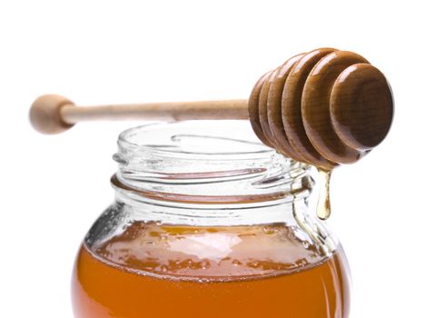 Jar of honey with a wooden drizzler on top. Isolated on white background.