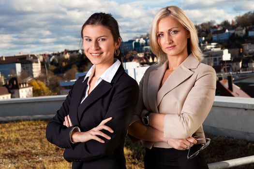 Two confident beautiful businesswomen standing ouside and smiling