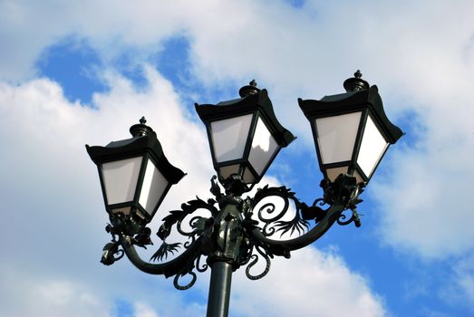 Triple beautiful classic forged lantern in blue cloudy sky on background