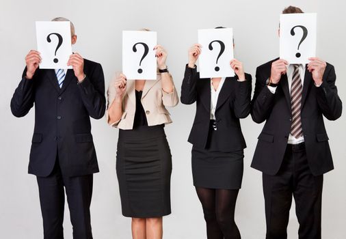 Group of unidentifiable business people hiding under question marks