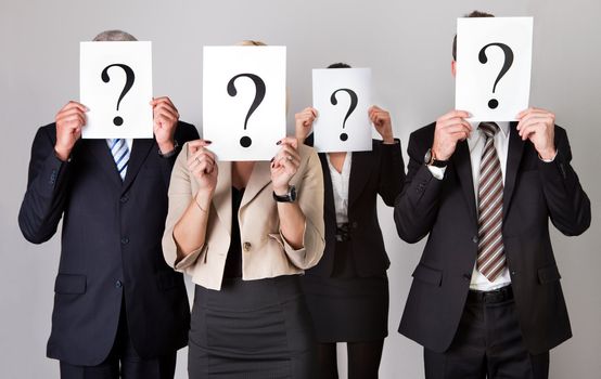 Group of unidentifiable business people hiding under question marks