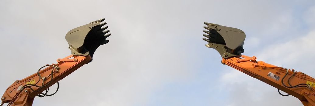 two excavator's shovels over grey sky