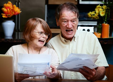Senior couple at home reacting to many bills