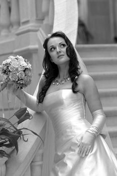 Half body portrait of beautiful young adult bride holding bouquet of flowers, stood in stairs.