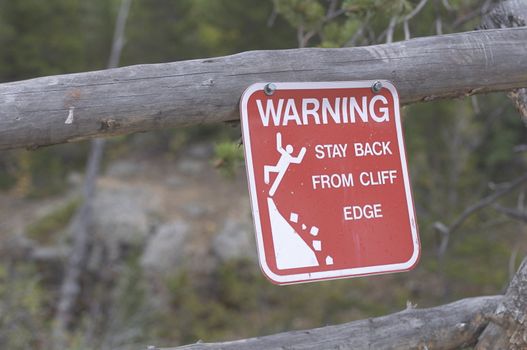 A metal sign warns of the danger of getting too close to the cliff.