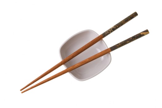 Two wooden chopsticks on white saucer. Sticks are decorated with temple theme ornamentation. Isolated on white