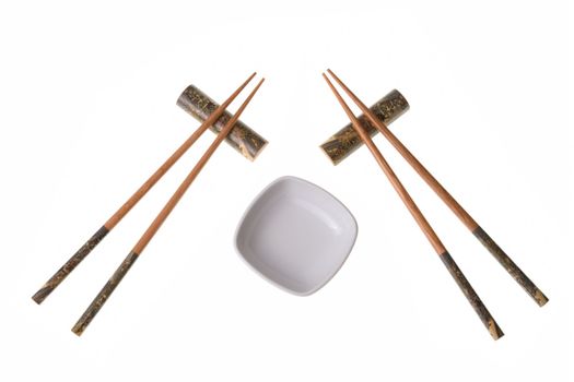 Two pairs of wooden chopsticks and white empty saucer. Sticks are decorated with temple theme ornamentation. Isolated on white