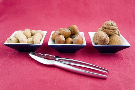 walnuts, hazelnuts and peanuts in three bowls on red background