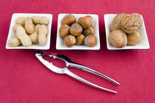 walnuts, hazelnuts and peanuts in three bowls on red background