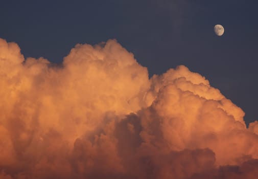 Puffy orange clouds and the moon in the background. 