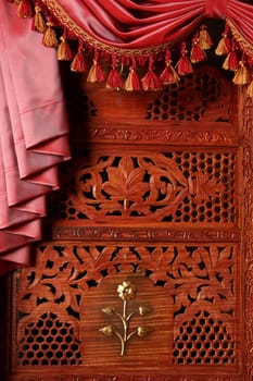 Fragment of the Indian carved wooden screen with a red curtain