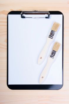 Two brushes are located on blank clipboard. The photo is intended for business connected with painting and dressing.