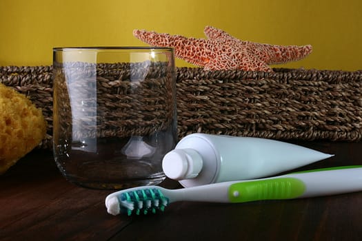 Tooth-paste and brush against a wattled basket with a starfish and a glass for mouth rinsing.