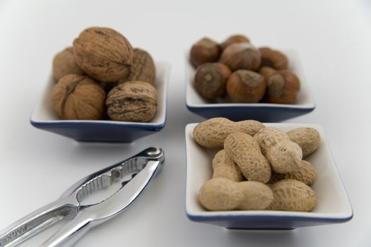 walnuts, hazelnuts and peanuts in three bowls on white background