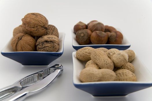 walnuts, hazelnuts and peanuts in three bowls on white background