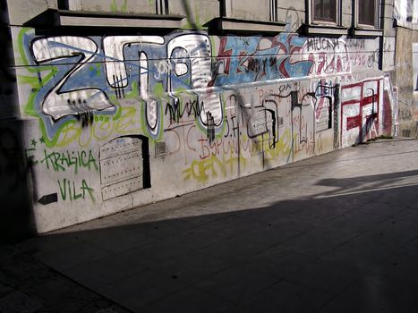 Detail of wall coloured with graffiti and alight with sun.